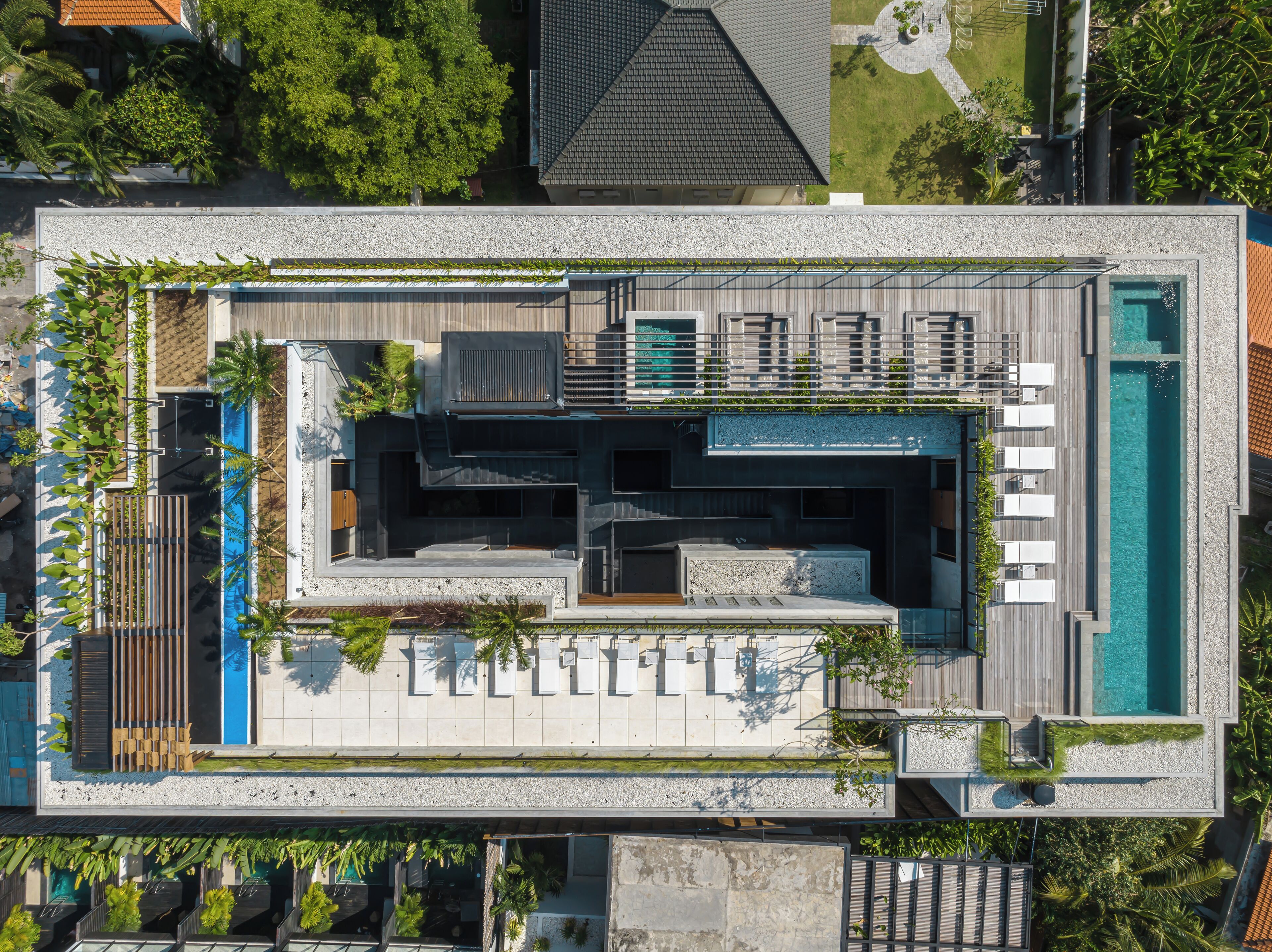Vue aérienne d’un hôtel moderne doté d’une piscine sur le toit, d’un espace extérieur aménagé et d’une végétation luxuriante.