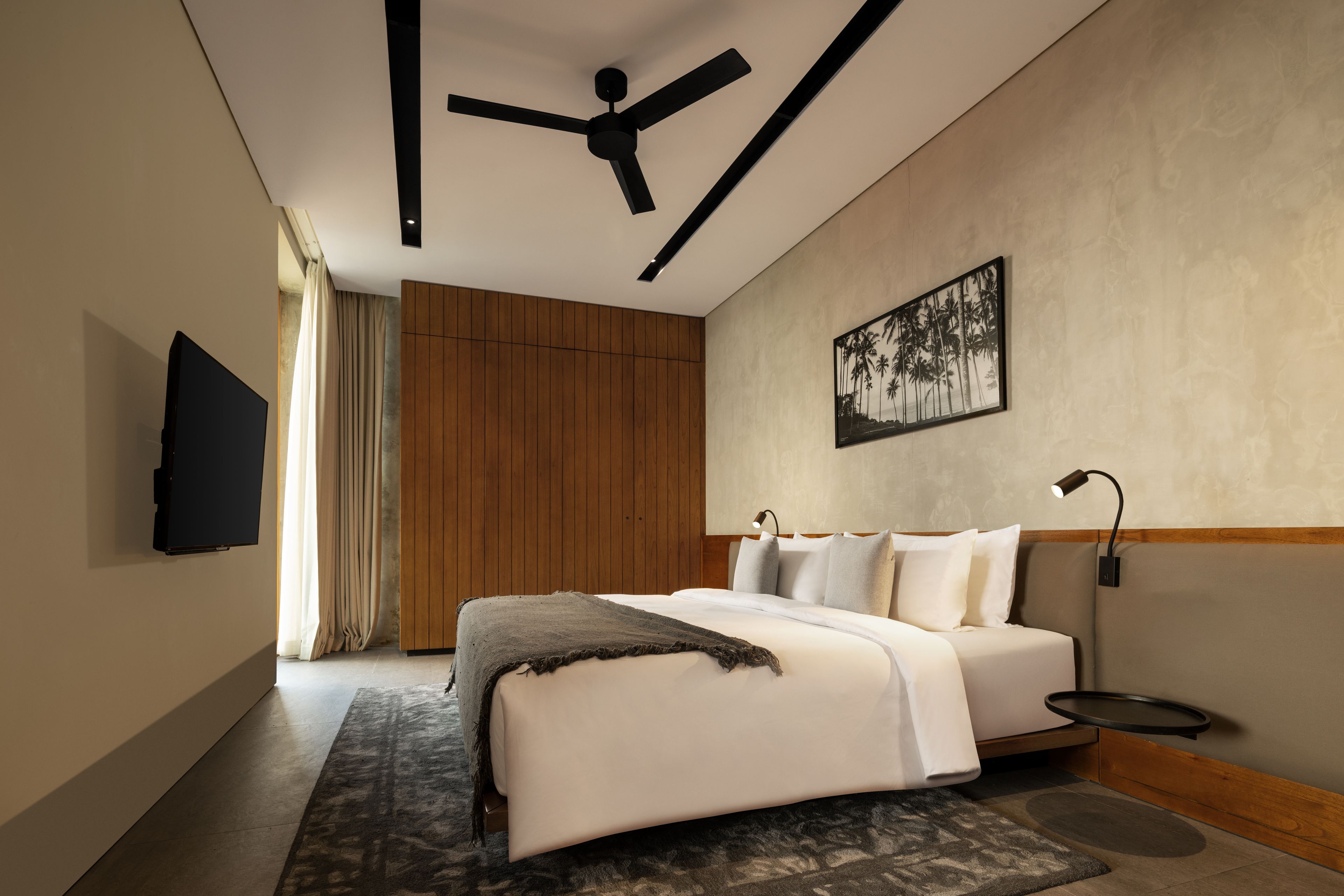 A modern bedroom with a bed, a ceiling fan, a mounted TV, and a framed picture on the wall.