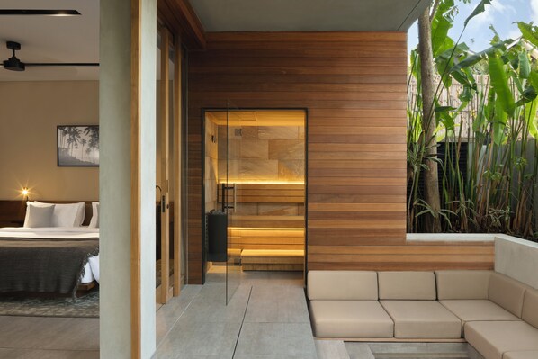 A modern interior with a wooden wall, a glass door leading to a bathroom, and a seating area with a view of tropical plants.