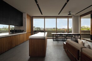 A modern kitchen with a central island, wooden cabinetry, and a large window offering a view of the cityscape. - Body Factory Lifestyle Residence Canggu (Canggu)