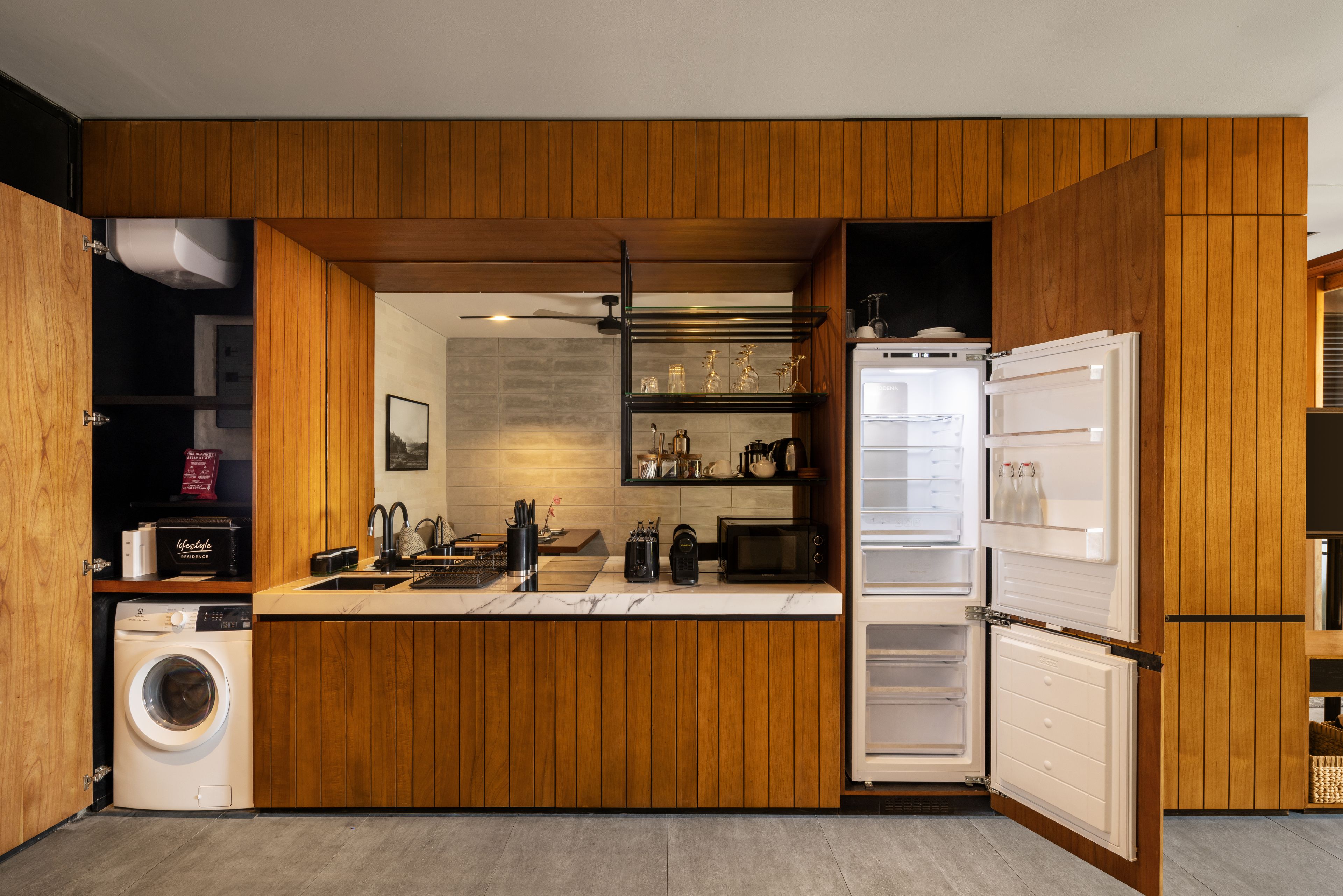 A compact kitchen with wooden cabinetry, a built-in washing machine, a microwave, and a refrigerator.