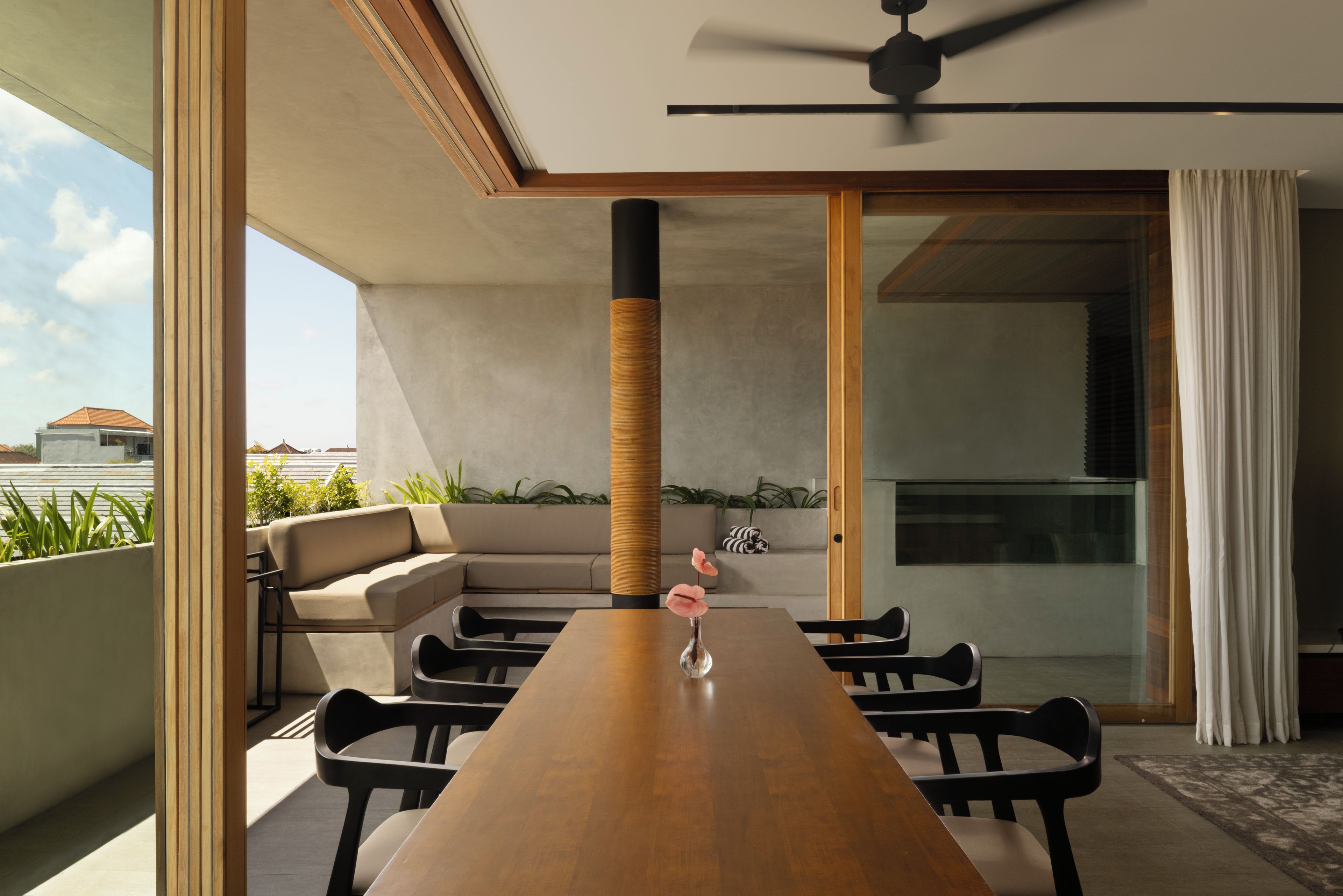 Un comedor moderno con una larga mesa de madera, sillas negras, un ventilador de techo y vista al cielo.