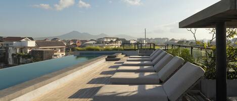 A rooftop pool area with lounge chairs and a view of a mountain range.