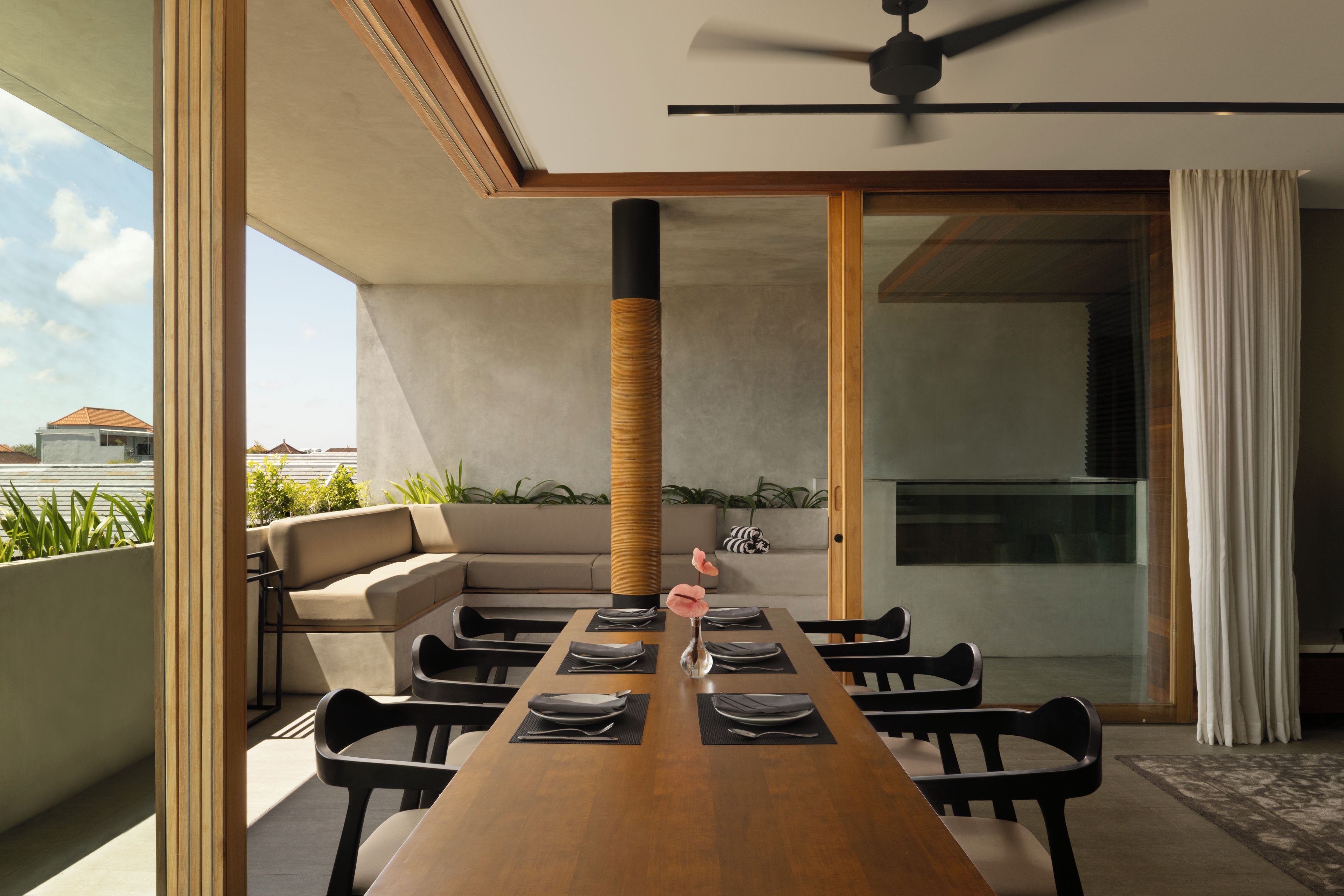 Un espace repas moderne avec une longue table en bois, des chaises noires et un ventilateur de plafond.