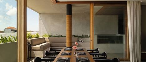 Un'area pranzo moderna con un lungo tavolo in legno, sedie nere e una ventola a soffitto.