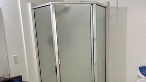 Et badeværelse med glasvægsbrusebad, en hvid vask, et toilet og en skraldespand.