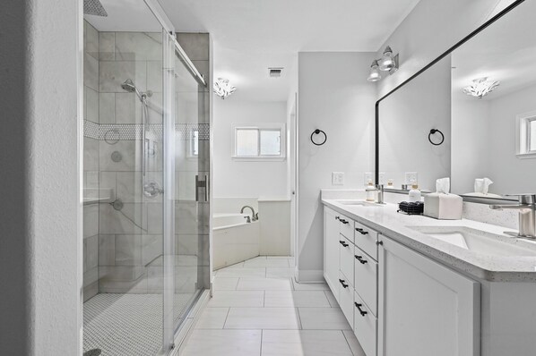 A modern bathroom with a glass-enclosed shower, a bathtub, and a large mirror.