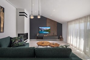 Una sala de estar moderna con un televisor de pantalla plana grande, un sofá de color oscuro y una mesa de centro de madera.