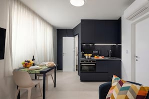 A modern kitchen with dark cabinets, a dining area with a table set for two, and a colorful cushion on a chair.