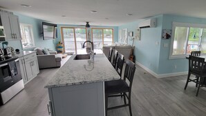A spacious kitchen with a large island, a dining area with chairs, and a view of a water body. - Newly Renovated, Lakefront, Dog Friendly Cottage, Sand Lake, Harrison (Harrison)