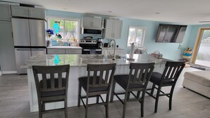 A modern kitchen with a central island, bar stools, and a view of the outside. - Newly Renovated, Lakefront, Dog Friendly Cottage, Sand Lake, Harrison (Harrison)