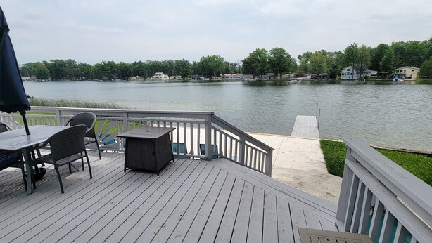 A deck with outdoor furniture, a small table, and a covered umbrella. - Newly Renovated, Lakefront, Dog Friendly Cottage, Sand Lake, Harrison (Harrison)