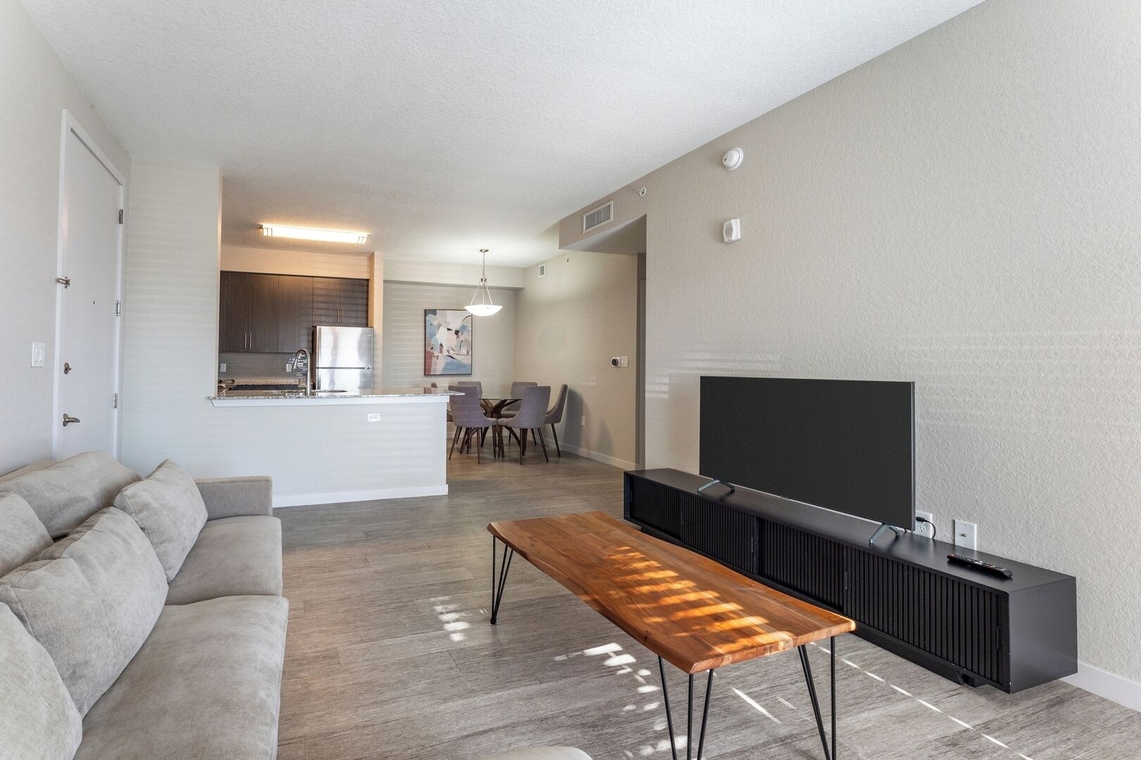 A modern living room with a sofa, a wooden coffee table, a TV on a black stand, and a kitchen in the background.
