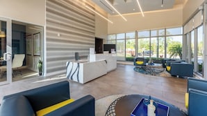 A modern reception area with a marble counter, seating with yellow cushions, and large windows offering a view of the outdoors. - Daytona 2BR Getaway Parking Family & Pet-friendly (Daytona Beach)