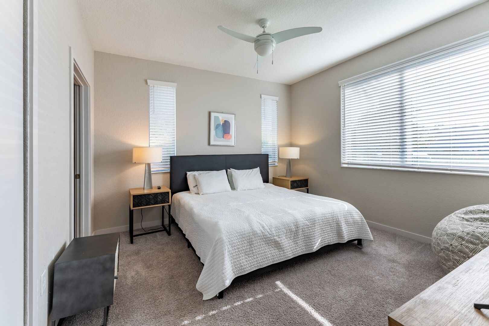 A bedroom with a bed, two bedside tables, a ceiling fan, and a window with blinds.