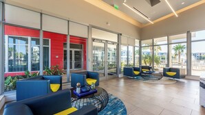 A modern hotel lobby with blue and yellow seating, large windows, and a red accent wall. - Daytona 2BR Getaway Parking Family & Pet-friendly (Daytona Beach)