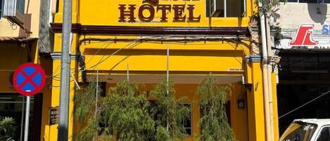 Een geel gebouw met een bord waarop 'QISH HOTEL' staat en een verbodsbord voor parkeren.