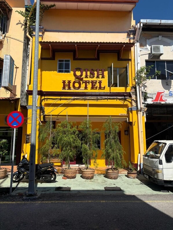 Un bâtiment jaune avec une enseigne indiquant « HÔTEL QISH » et un panneau interdisant le stationnement.