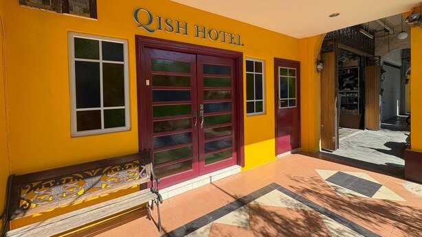 The exterior of Qish Hotel with a yellow facade, a large red door, and a bench outside. - Qish Hotel (Malacca City)