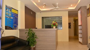 A hotel reception area with a reception desk, a black leather sofa, a potted plant, and a ceiling fan. - Qish Hotel (Malacca City)