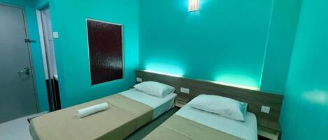 A room with two beds, a wall-mounted light, and a door.
