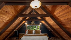 A bedroom with a sloped ceiling, a bed with pillows, a window, and a hanging light fixture. - Charming, rustic cabin on the golf course (Packwood)