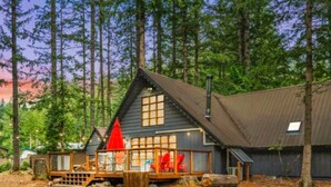 A cabin with a wooden deck, large windows, and a red umbrella. - Charming, rustic cabin on the golf course (Packwood)