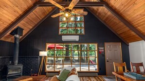 A cozy loft bedroom with a sloped ceiling, a large window overlooking a deck, a fireplace, and a ceiling fan. - Charming, rustic cabin on the golf course (Packwood)
