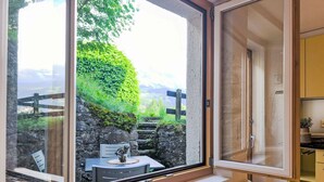 A room with a large window overlooking a stone wall and greenery, a small table with a plant, and a yellow cabinet. - Galliweidli by Interhome (Wengen)