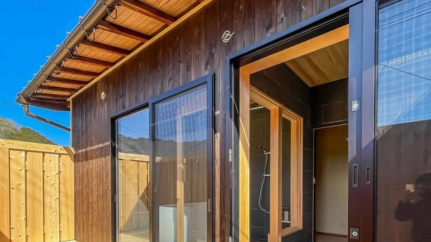 A modern wooden building with large sliding glass doors leading to a shower area.