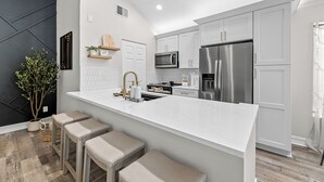 Una cocina moderna con armarios blancos, electrodomésticos de acero inoxidable y una isla central con taburetes.