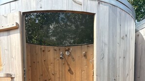 A wooden sauna with a door, a showerhead, and a small step inside.