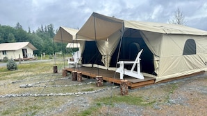 A large tent with a wooden deck and white chairs, set in a grassy area with trees in the background.