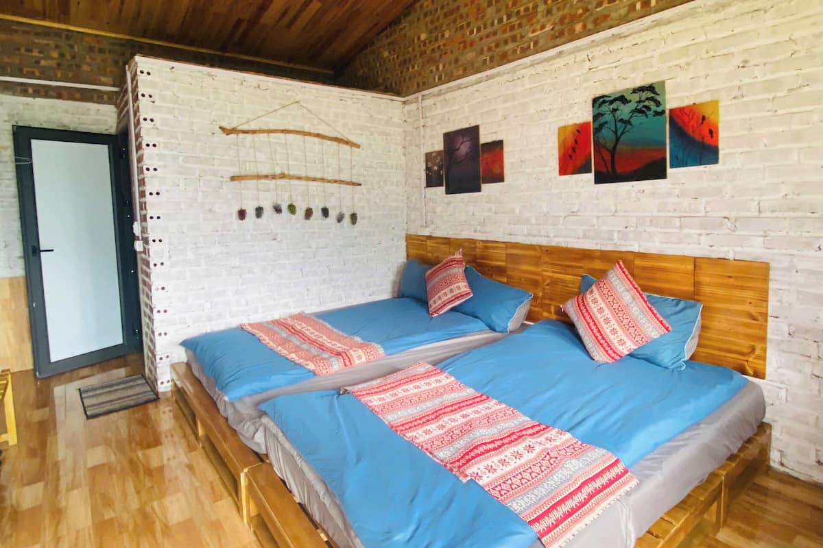 A room with two beds, wooden flooring, a brick wall, and a wooden ceiling.