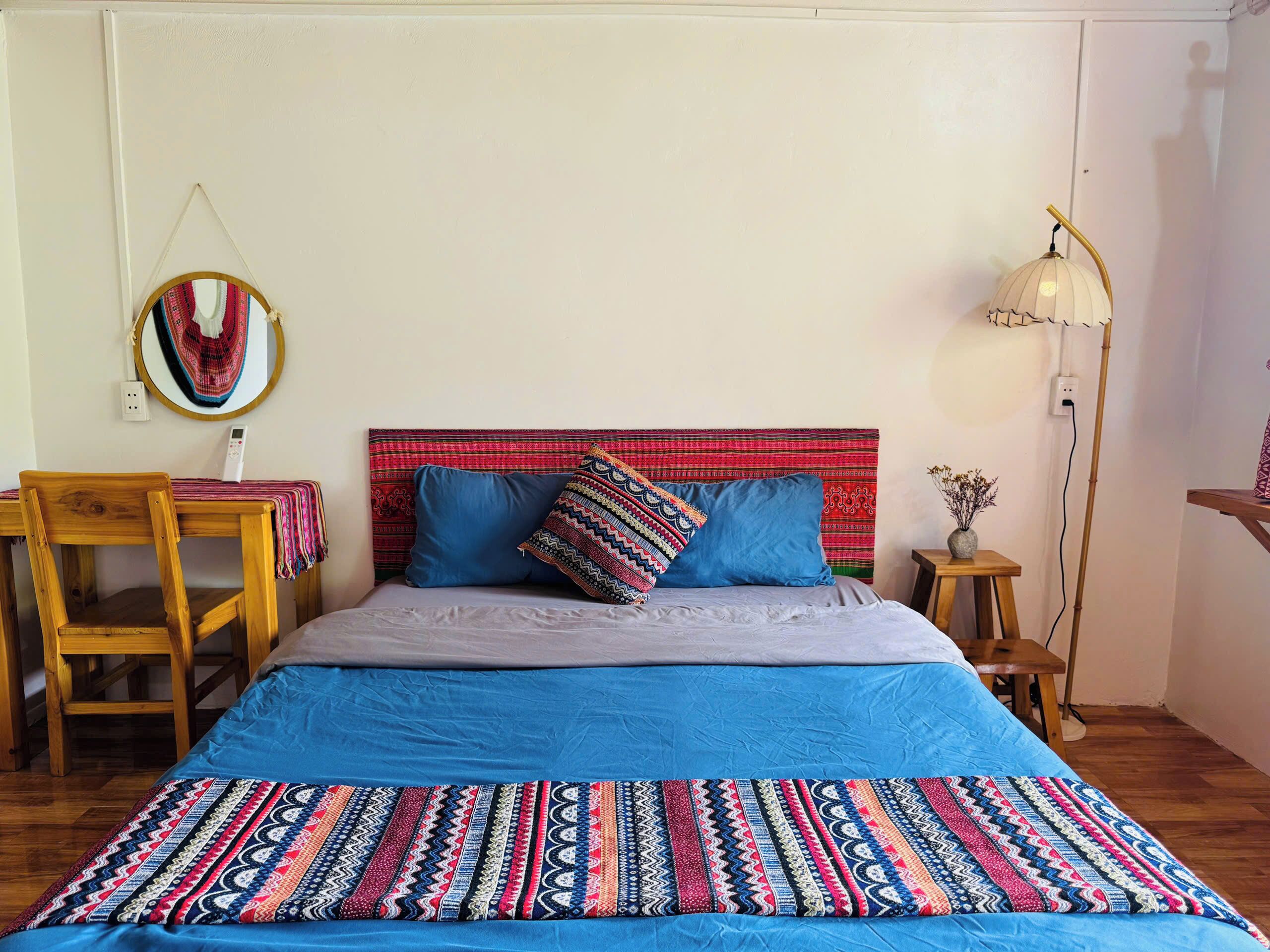 Una cama con colcha estampada, dos almohadas, una mesita de noche con lámpara, una silla y un adorno en la pared.