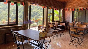 A spacious room with large windows, wooden tables, and chairs. - The Link Farmstay (Sa Pa)