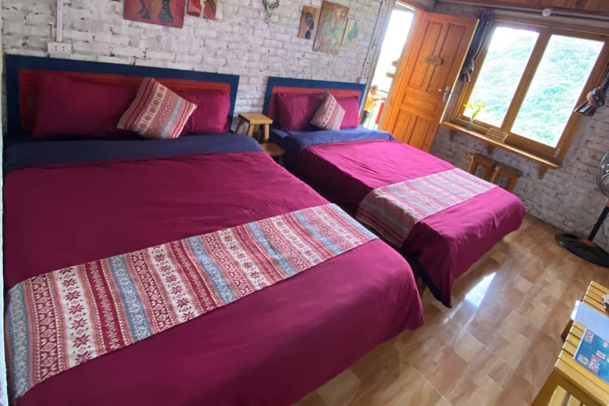 A room with two beds, wooden flooring, a brick wall, and artwork.