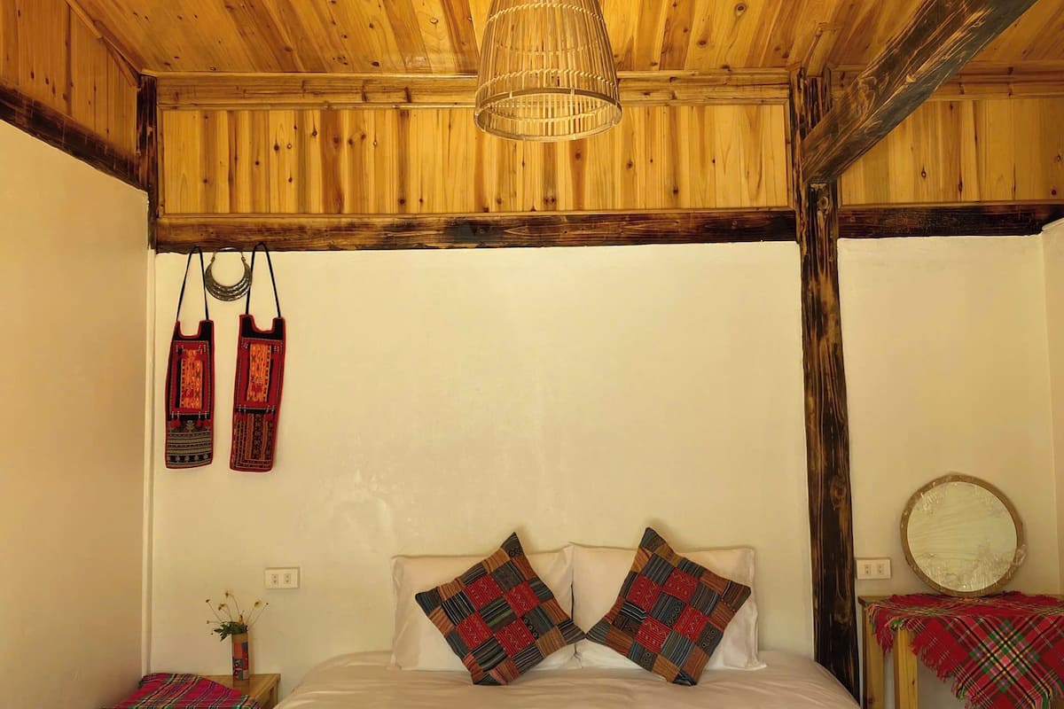 A wooden ceiling with a woven light fixture, a bed with patterned pillows, and a mirror on a bedside table.