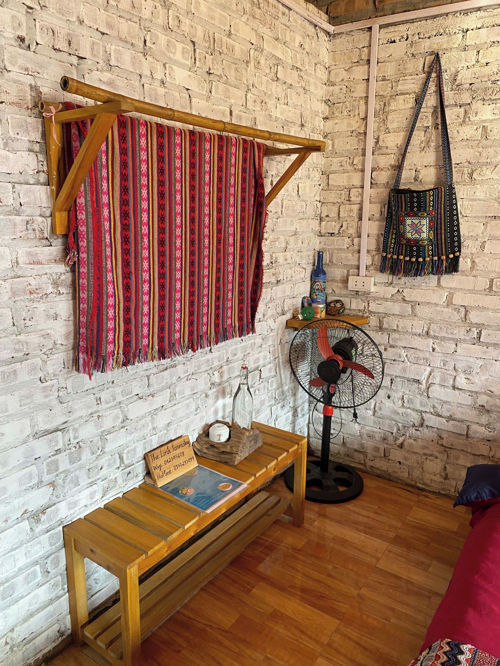 A room with a brick wall, a wooden bench, a fan, and a hanging bag.