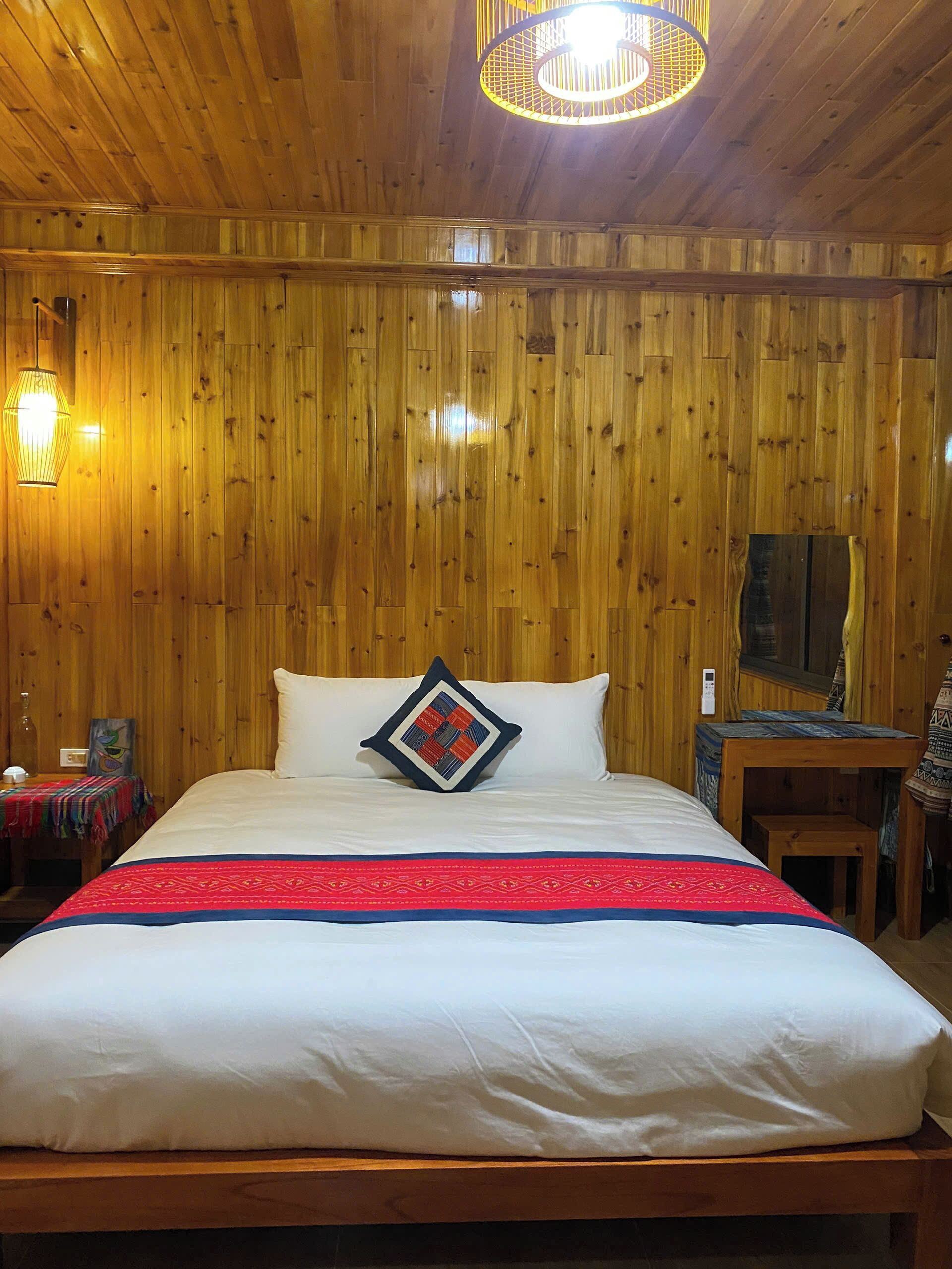 A wooden-paneled room with a bed, a table, and a lamp.