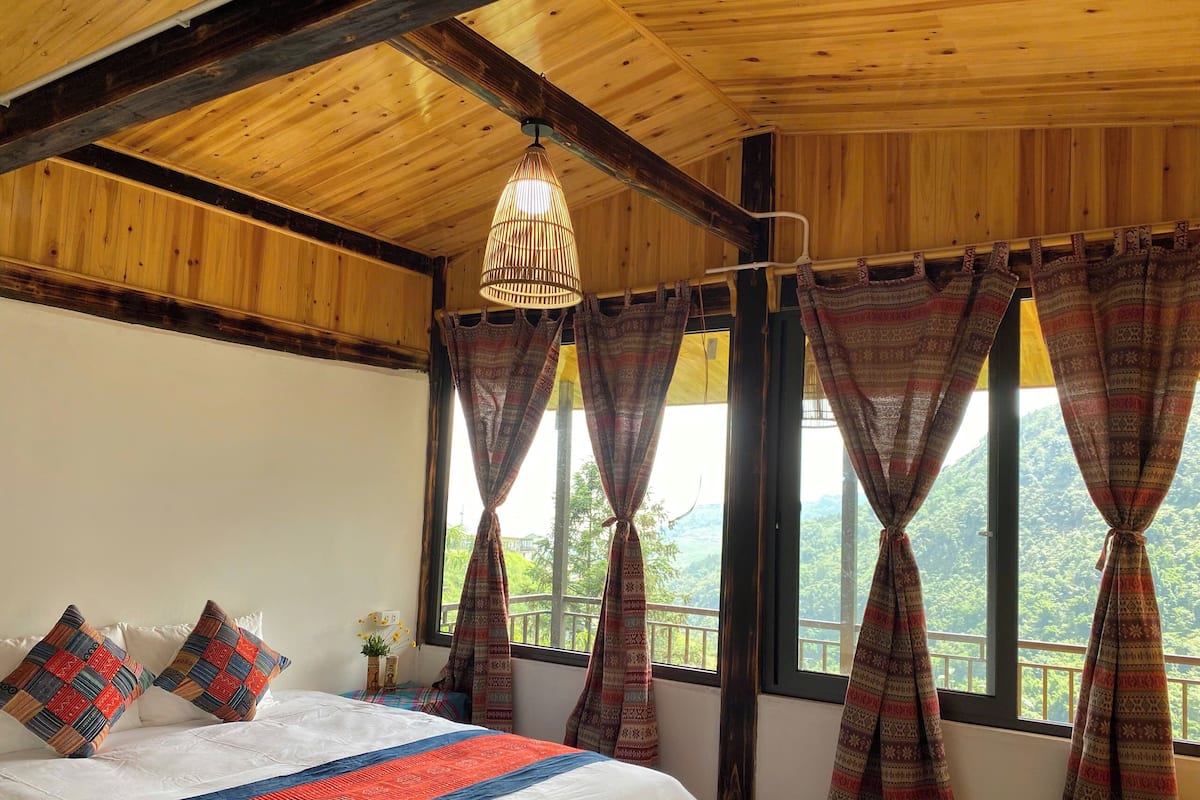 A wooden room with a bed, patterned curtains, and a view of greenery.