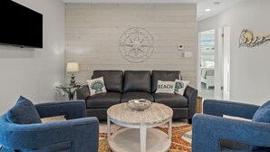 Un salon moderne avec un canapé en cuir, deux fauteuils bleus, une table basse et une décoration murale représentant une boussole.