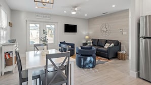 Un salon moderne comprenant un coin repas, un canapé gris, un téléviseur fixé au mur et une grande fenêtre.