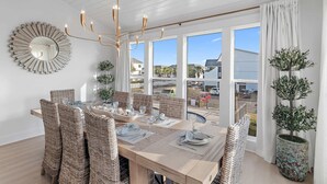 A dining area with wicker chairs, a wooden table, a chandelier, and large windows with curtains. - Steps to the Private Beach, BRAND NEW renovations, 3 Bikes - 30A Sun Joy (Santa rosa beach)