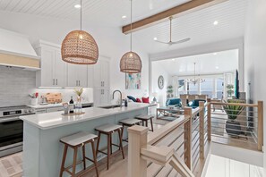 Une cuisine moderne avec des meubles blancs, un îlot central doté de tabourets et un éclairage suspendu.