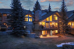 A multi-story lodge with a stone facade, large windows, and a balcony overlooking a snowy landscape.