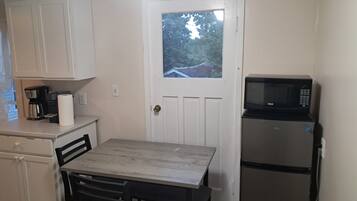 A compact kitchen with white cabinets, a wooden table, a black refrigerator, and a microwave.