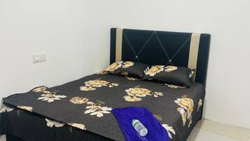 Uma cama com colcha florida, cabeceira com linhas diagonais e uma toalha azul na peseira.