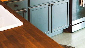 A kitchen with a wooden countertop, a stove, and cabinets.