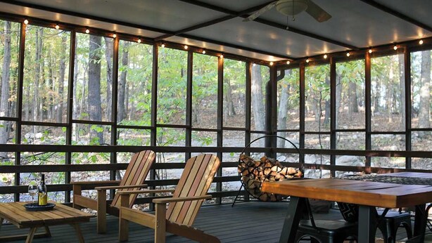 A covered outdoor area with wooden furniture, including chairs and a table, and a stack of firewood.